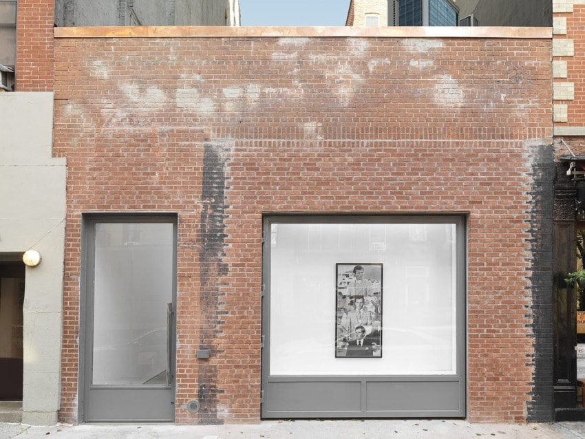Brick building facade with two large windows featuring a black and white photo displayed in the right window.