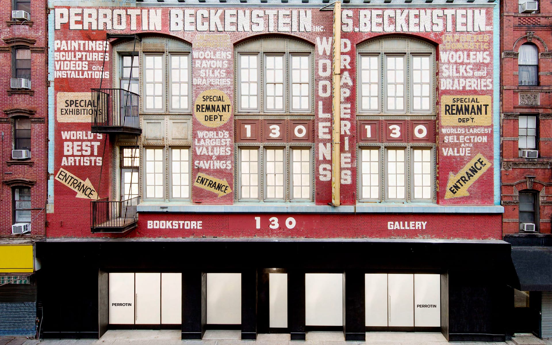 Vintage building with large painted advertisements for woolens and draperies, featuring Perrotin bookstore and gallery entrance.