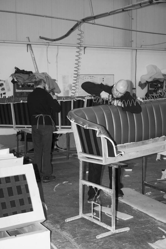 Craftsmen upholstering a sofa in a workshop, focusing on stitching and assembly in a detailed manufacturing process.