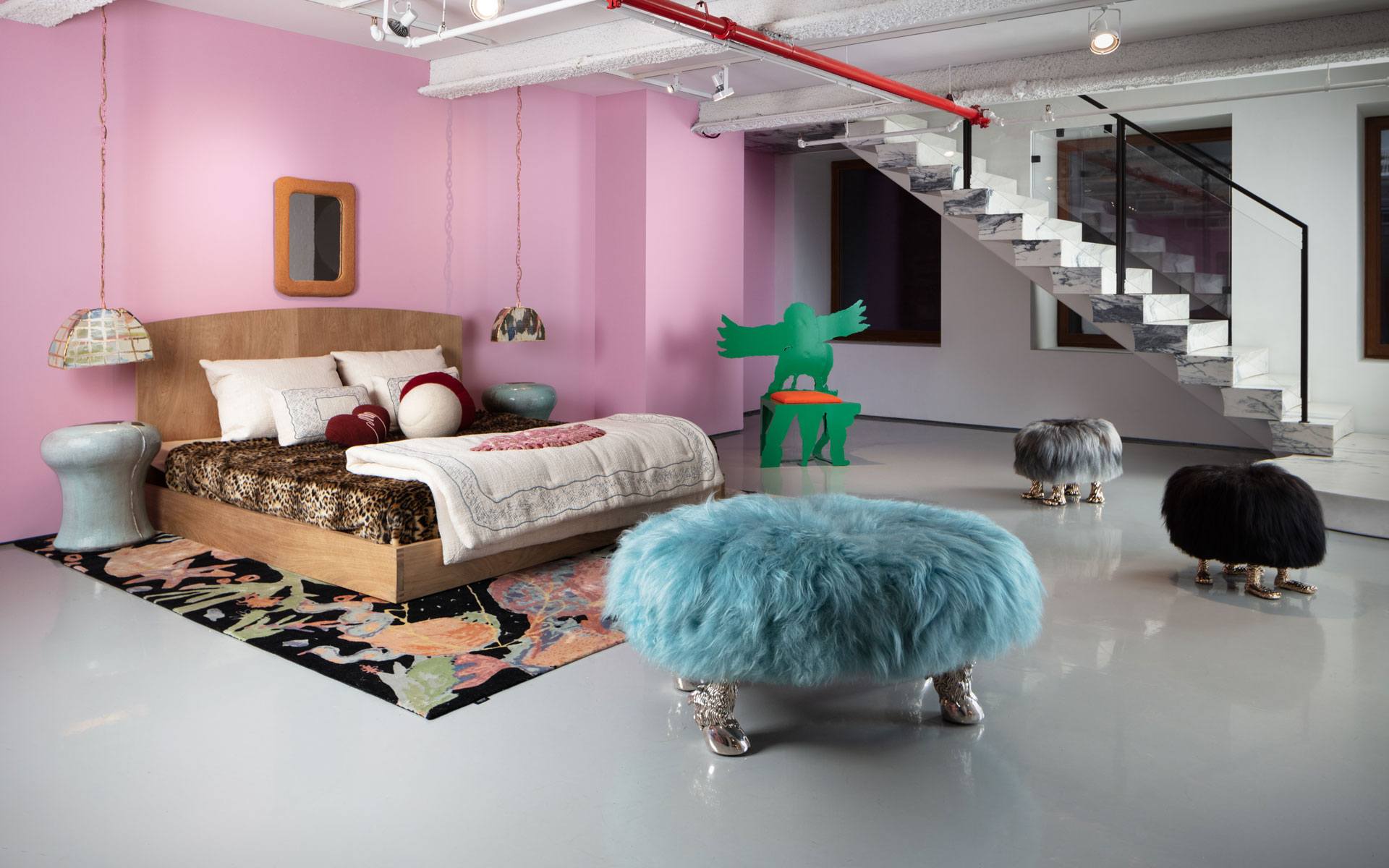Bedroom with pink walls, a wooden bed, eclectic decor including colorful furry stools, and an open staircase.