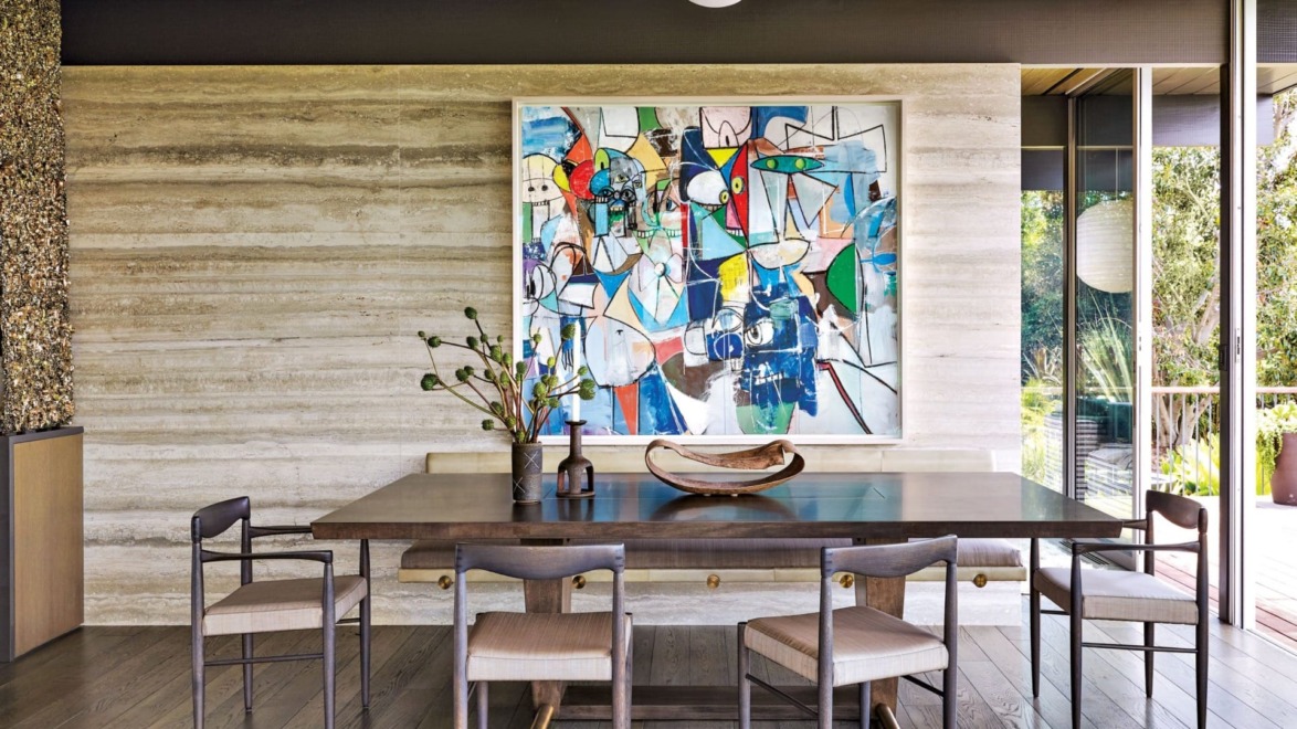 Modern dining room with wooden table, six chairs, abstract painting on wall, and large windows overlooking a garden.