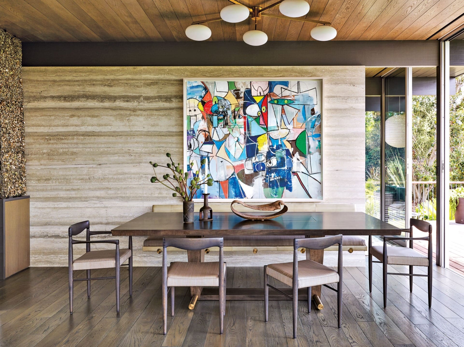 Modern dining room with wooden table, six chairs, abstract painting on wall, and large windows overlooking a garden.