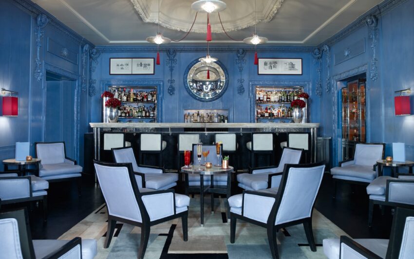 Luxurious lounge with blue walls, elegant chairs, and a fully stocked bar, creating a sophisticated atmosphere.