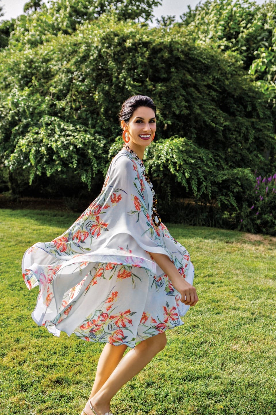 Woman twirls in a floral dress in a sunny garden, her smile vibrant and joyful against a backdrop of lush green foliage.