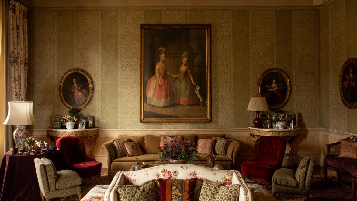 Elegant vintage living room with classic furniture, patterned wallpaper, and historical portraits on the walls.