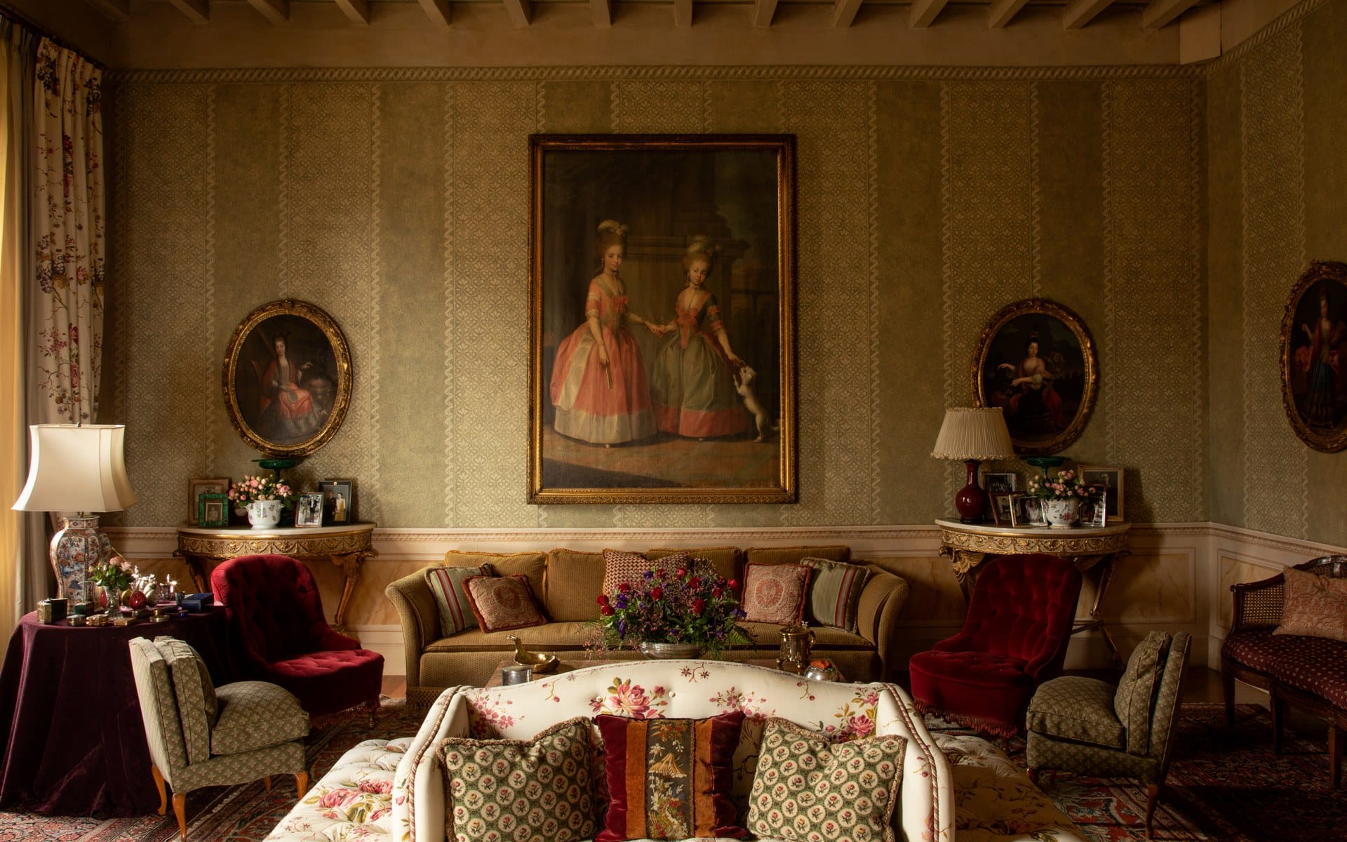 Elegant vintage living room with classic furniture, patterned wallpaper, and historical portraits on the walls.