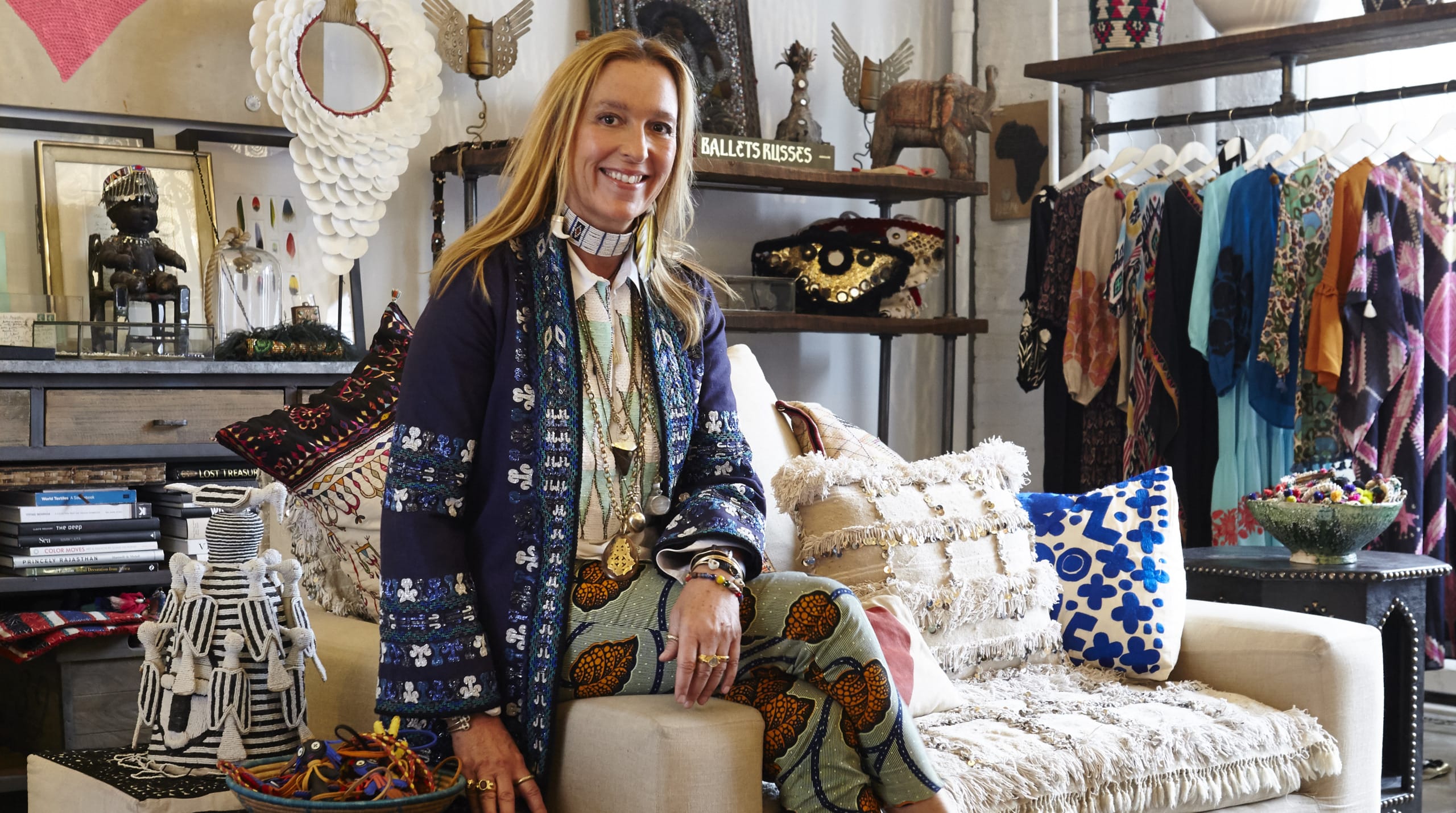 Person sitting in a colorful, eclectic room with various textiles, decorations, and a mannequin displaying patterned clothes.