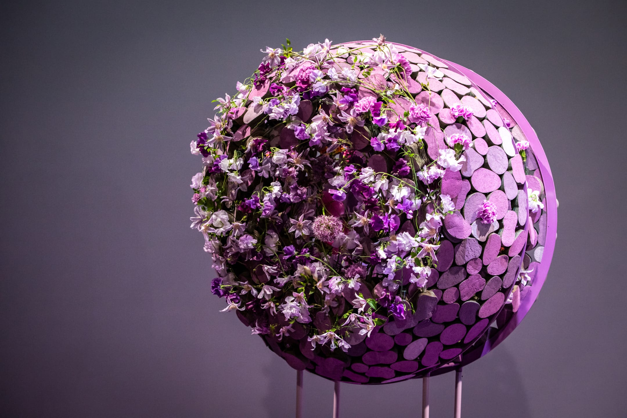 Sphere decorated with purple and white flowers on a stand against a dark background.