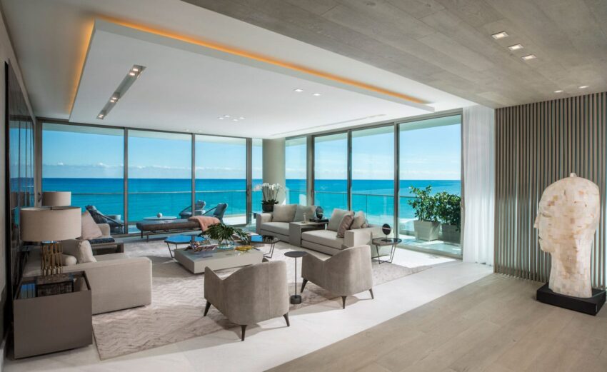 Modern living room with elegant furniture, ocean view through large windows, and stylish decor, including a sculpted head statue