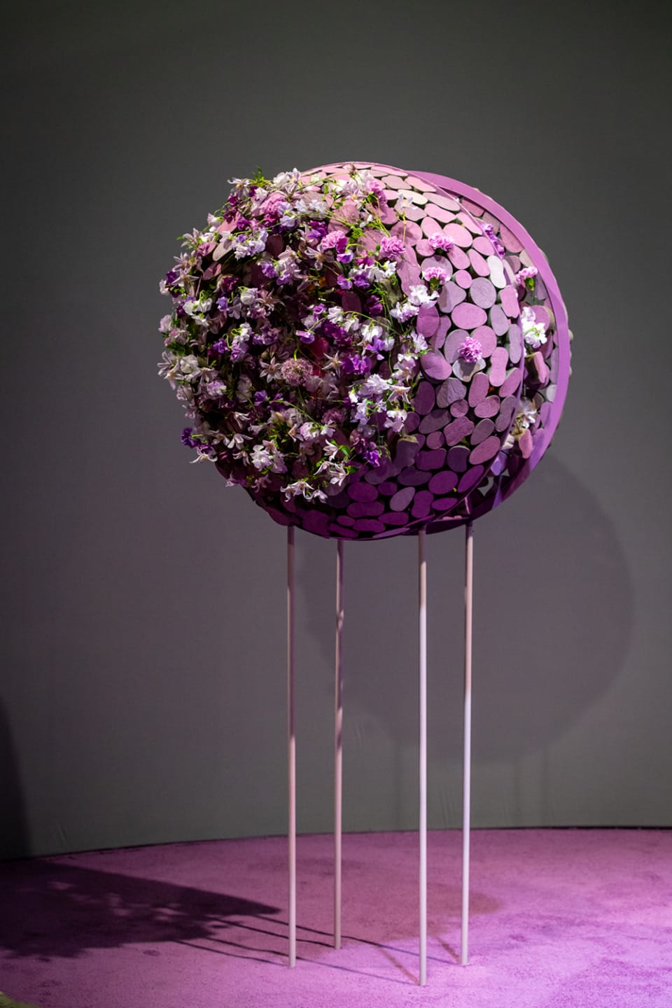 Spherical floral arrangement on tall stands with purple and white flowers against a muted green background.
