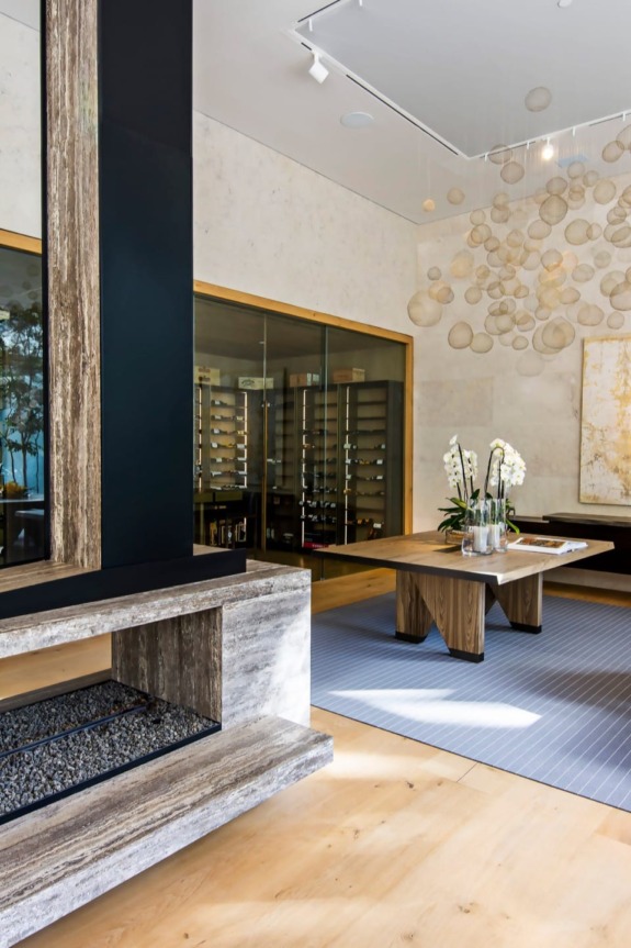 Modern wine cellar with a wooden table, orchid centerpiece, and glass-enclosed wine racks against a textured wall.