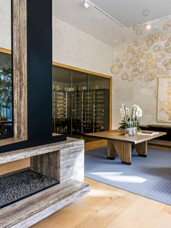 Modern wine cellar with a wooden table, orchid centerpiece, and glass-enclosed wine racks against a textured wall.