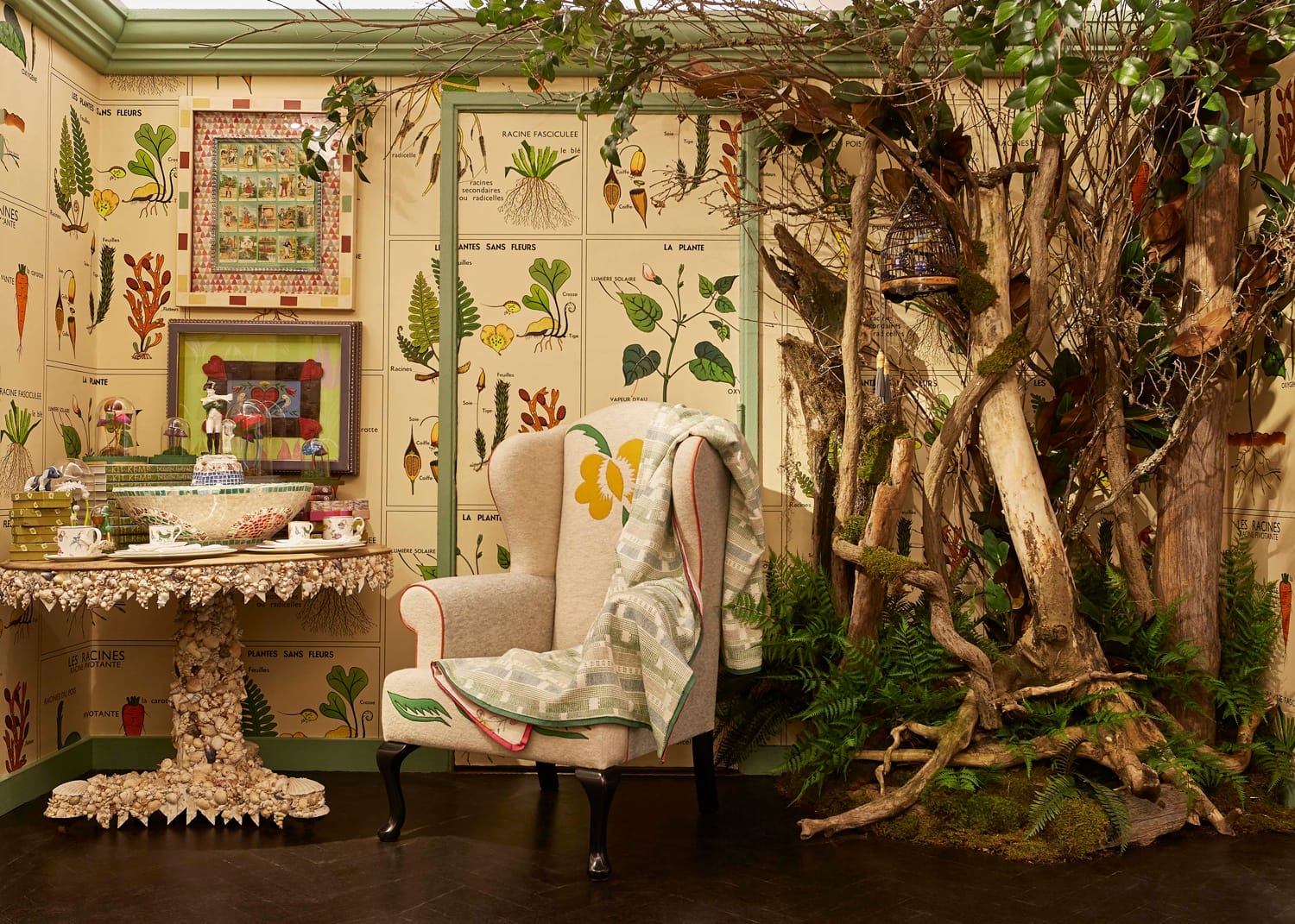 Cozy room with botanical wallpaper, a cushioned armchair, shell-decorated table, and a natural wood decoration.