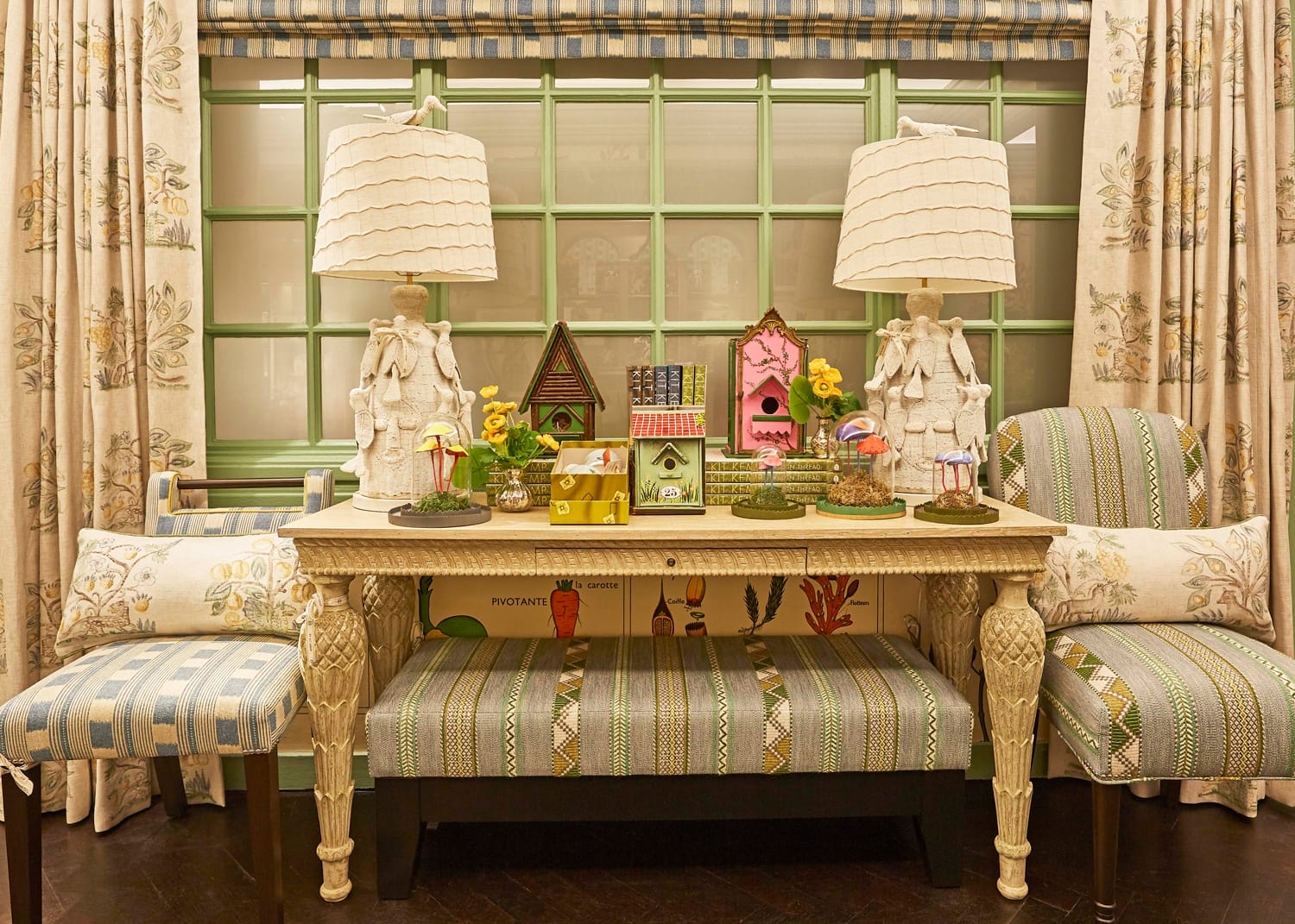 Decorative table with colorful birdhouses, lamps, and patterned chairs in a cozy, floral-themed room.