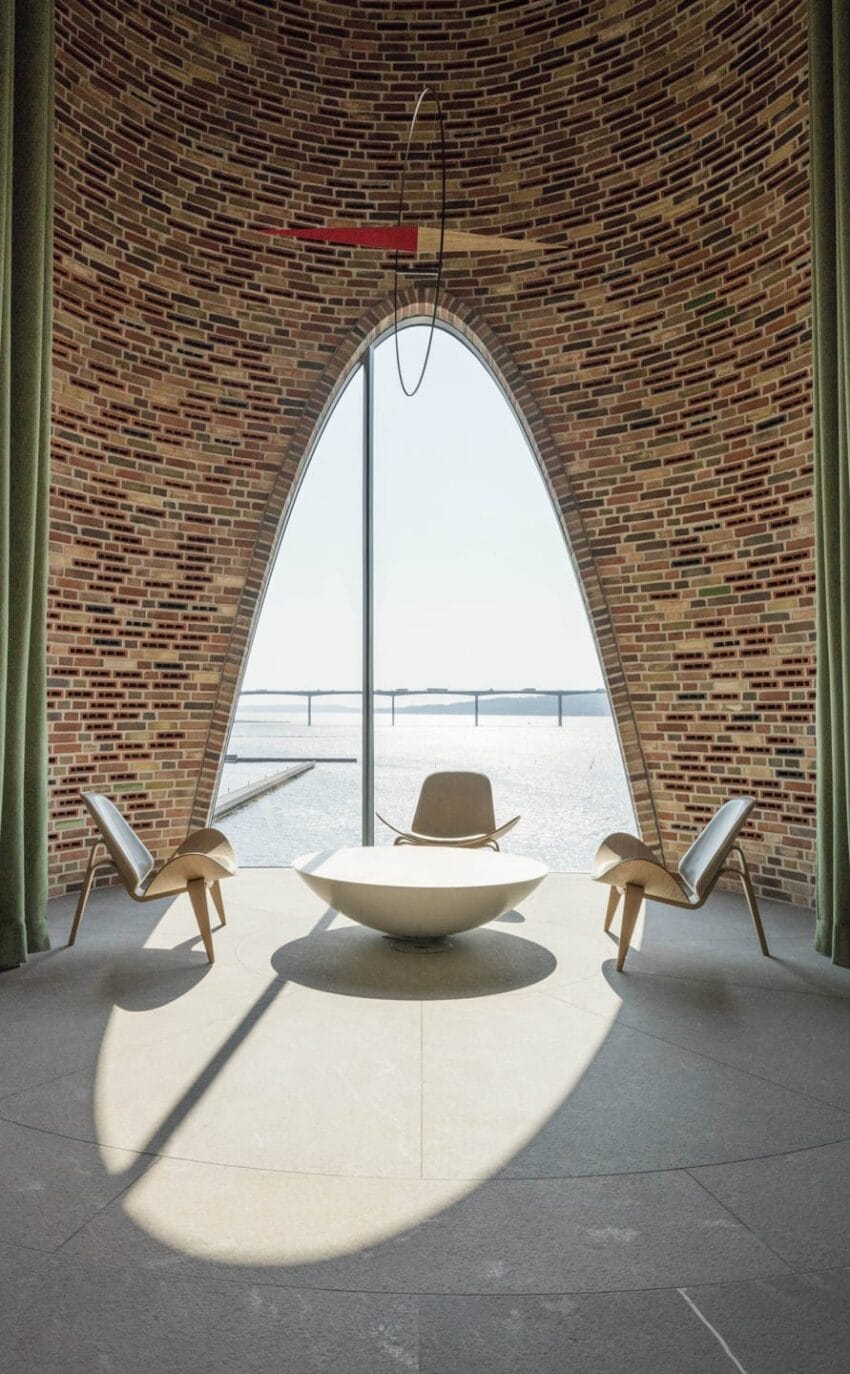 Modern interior with brick wall, three chairs around a round table, large window revealing a river view and distant bridge.