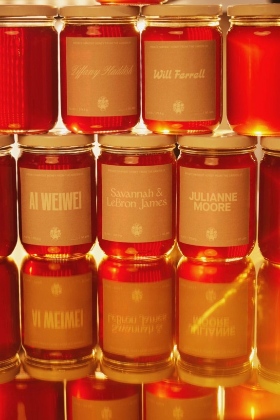 A stack of honey jars with labels featuring names of notable figures displayed artistically against a warm background.