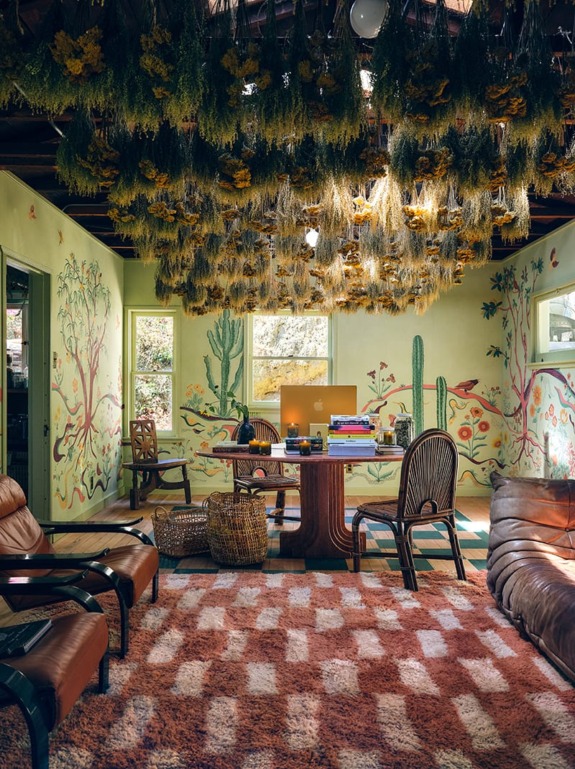 Eclectic room with hanging dried flowers, colorful murals, wooden furniture, and leather chairs creating a cozy atmosphere.