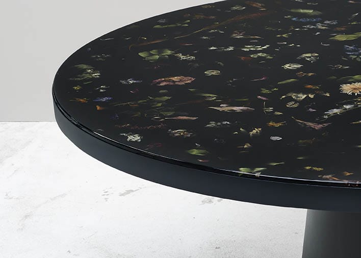 Round table with dark, nature-inspired surface pattern on light gray background.