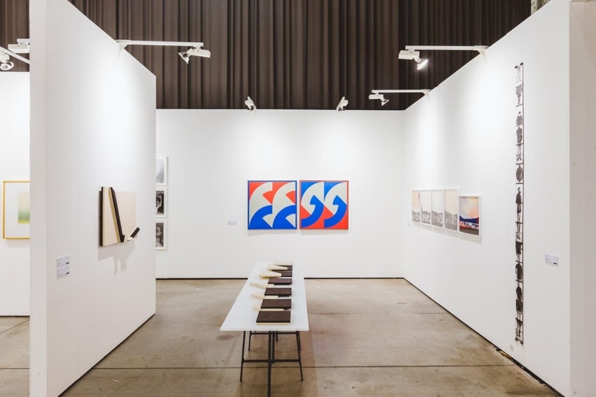 Contemporary art gallery interior with paintings on white walls and a table displaying artwork in the center.