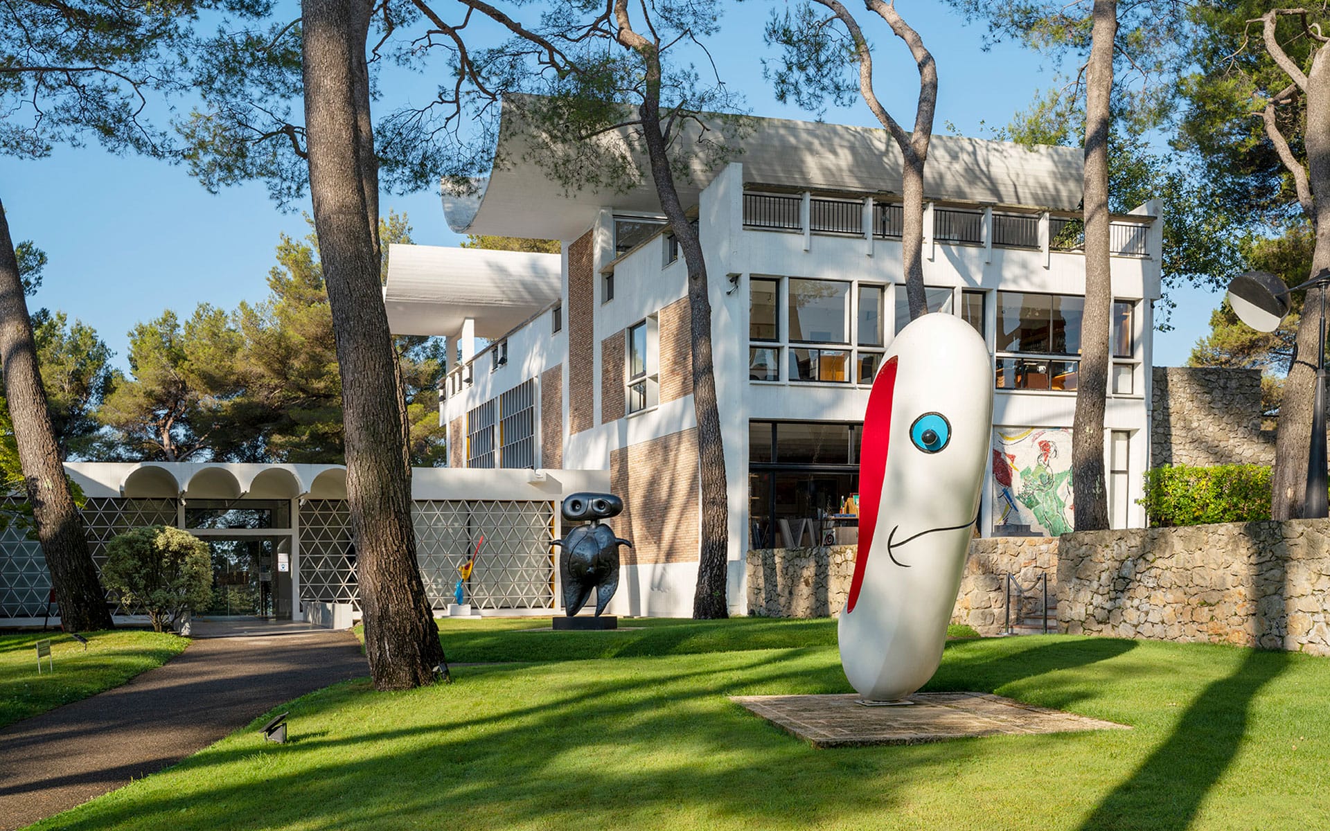 Modern art sculptures on a lawn in front of a contemporary white building surrounded by trees.
