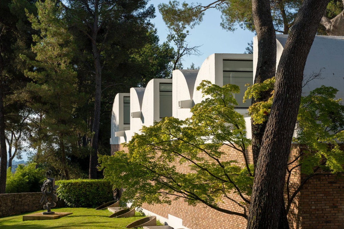 Modern building with large windows surrounded by trees and green lawn in a serene outdoor setting.