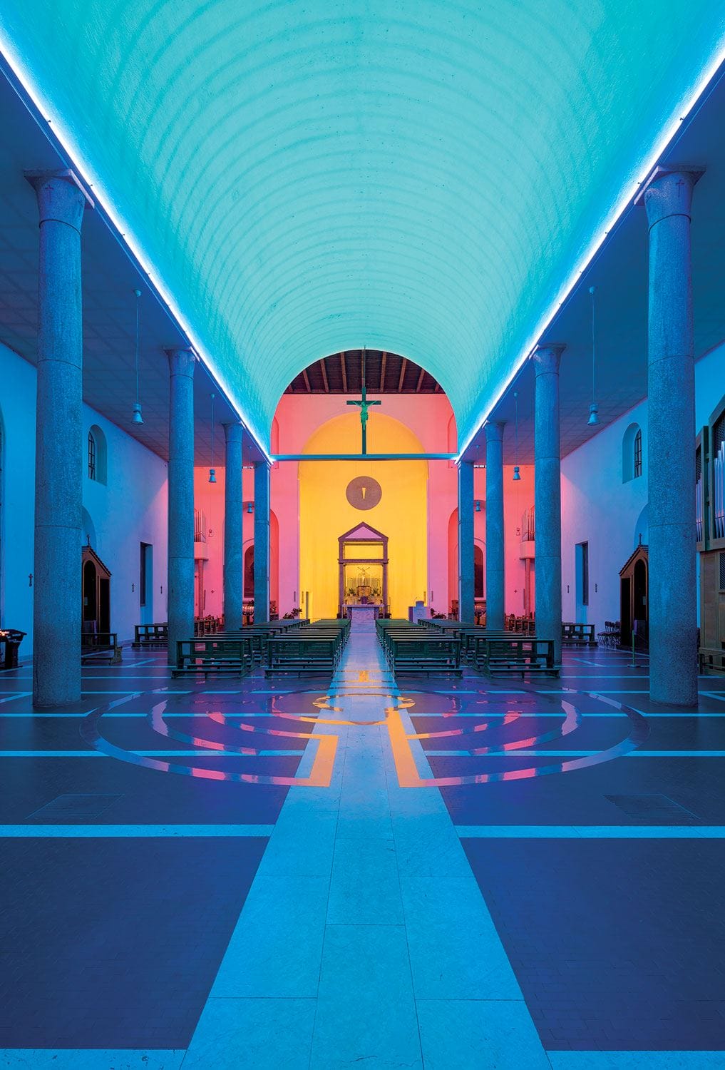 Colorfully lit modern church interior with arched ceiling, columns, and symmetrical design, showcasing vibrant blues and pinks.