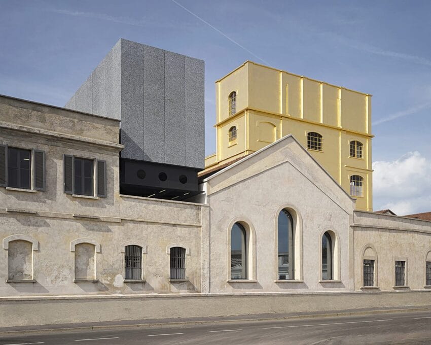 Industrial building with a modern extension, featuring a gray cube and a yellow structure under a clear sky.