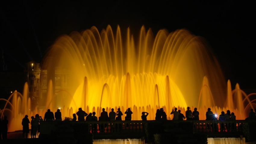 Silhouettes of people watching a vibrant nighttime fountain show with illuminated water arches.