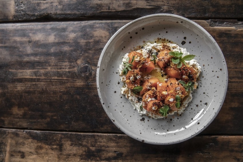 Plate of gourmet apricot dessert with cream and herbs on rustic wooden table