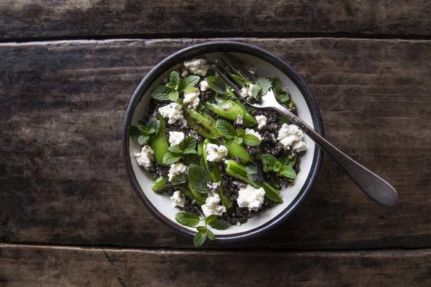 Salad with quinoa, cucumber, feta cheese, and mint leaves in a bowl on a rustic wooden table, with a fork inside.