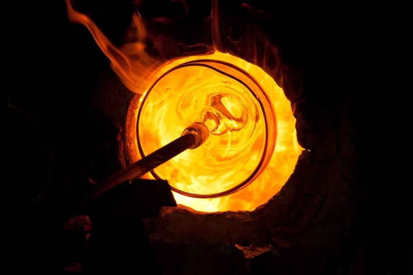 Glass being shaped in a hot furnace, glowing with intense orange flames, showcasing the glassblowing process.