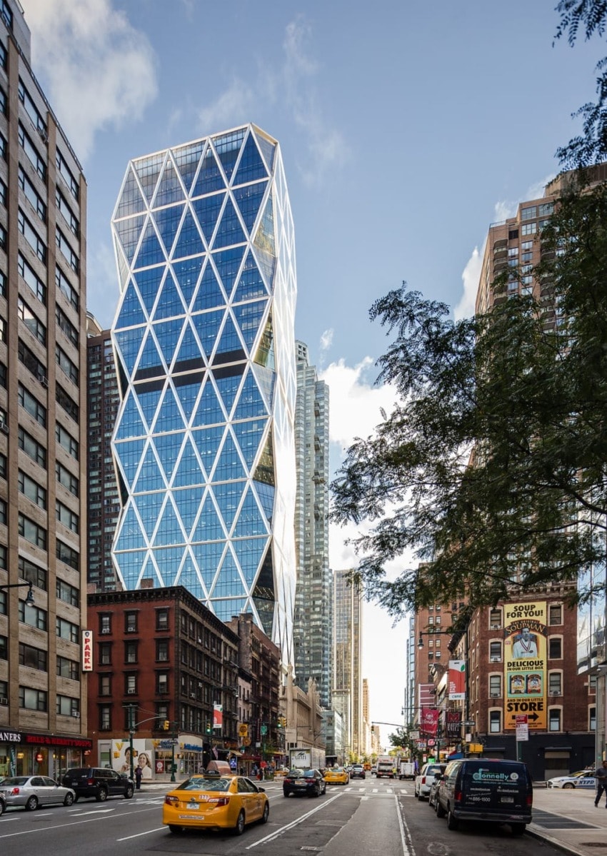 Modern skyscraper with diamond pattern facade on a busy city street lined with taxis and tall buildings, under a blue sky.