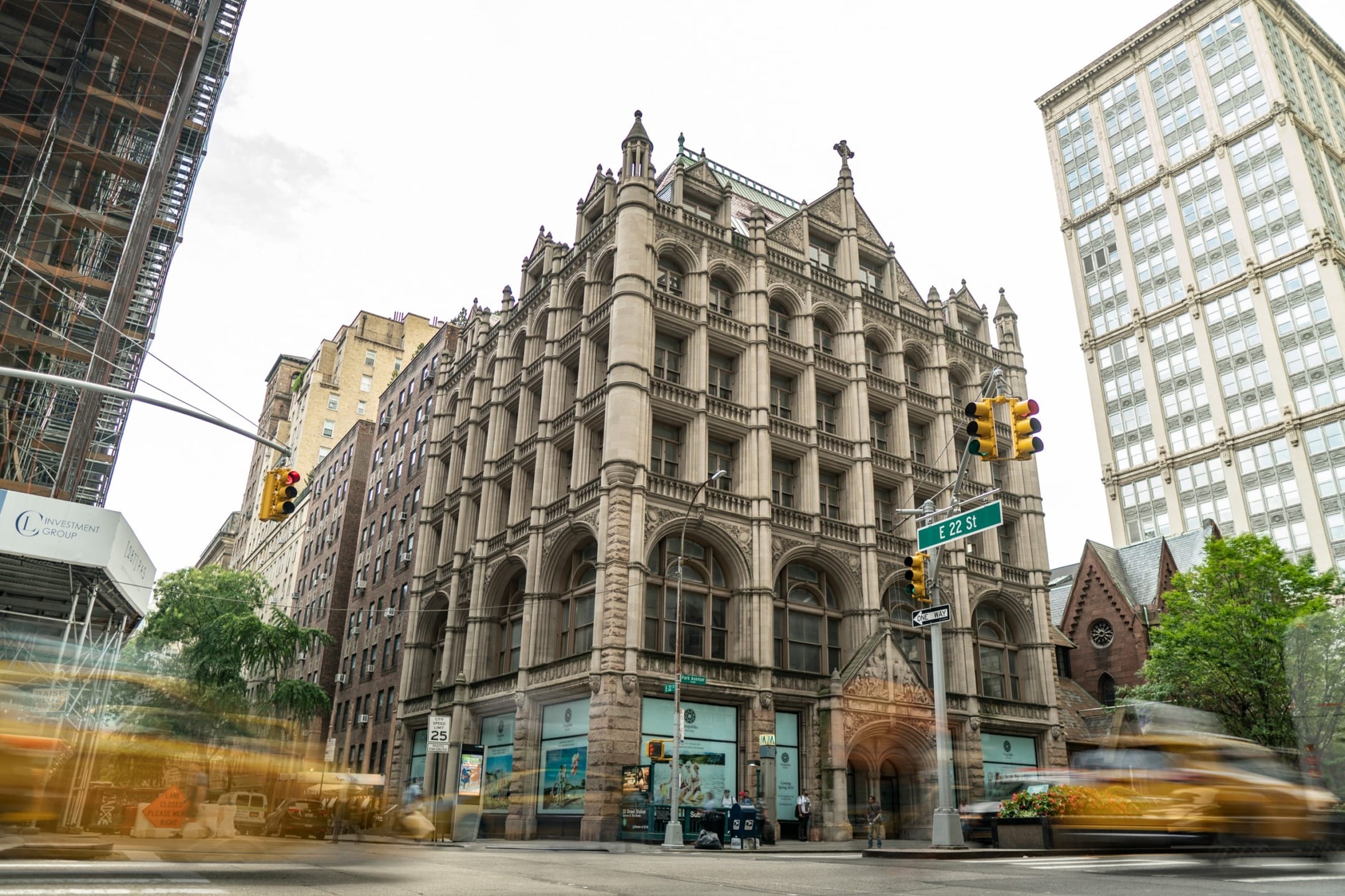 Historic Gothic-style building at a busy city intersection with blurred motion of cars and pedestrians.