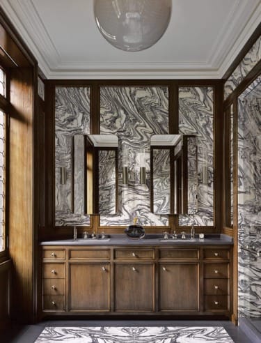 Luxurious bathroom with marbled walls, wooden cabinetry, double sinks, and large mirrors under a ceiling light fixture.