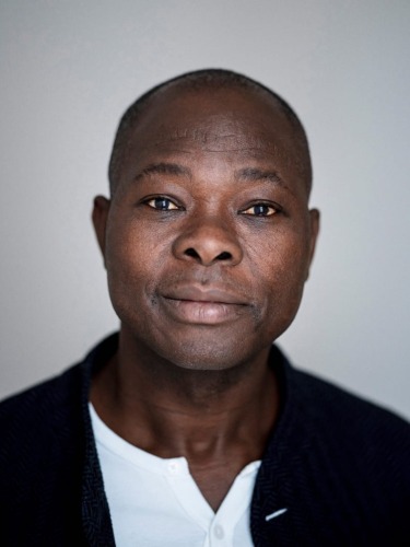 Smiling person in a dark jacket over a white shirt against a plain background