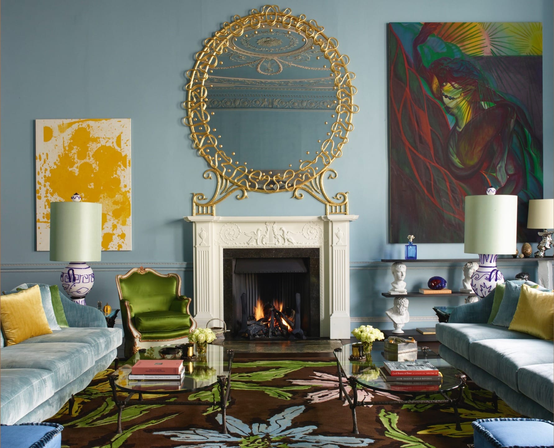 Luxurious living room with ornate mirror, colorful paintings, and vibrant furniture surrounding a cozy fireplace.