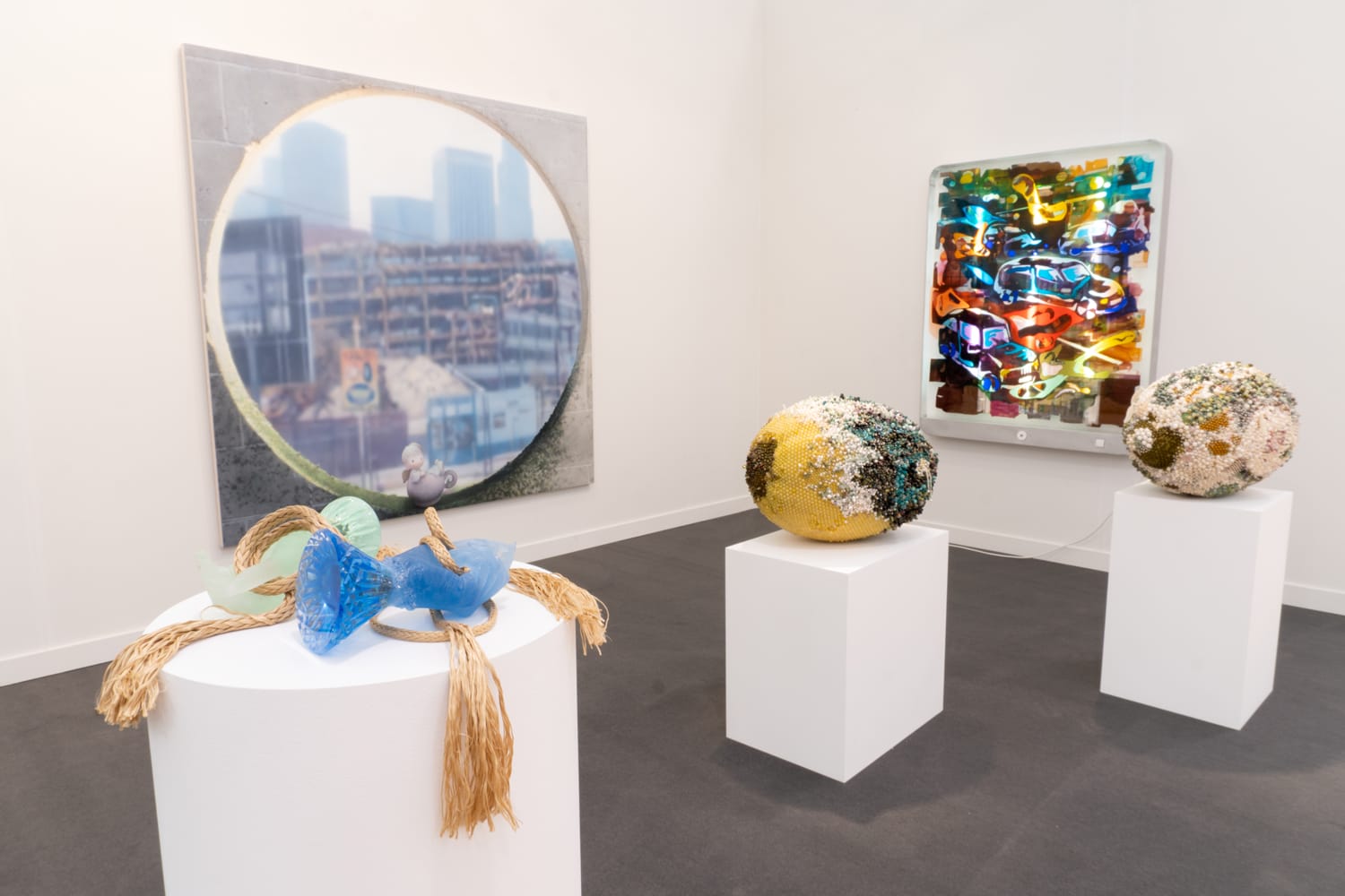 Contemporary art exhibit featuring a large blurred cityscape painting and colorful abstract sculptures on white pedestals.