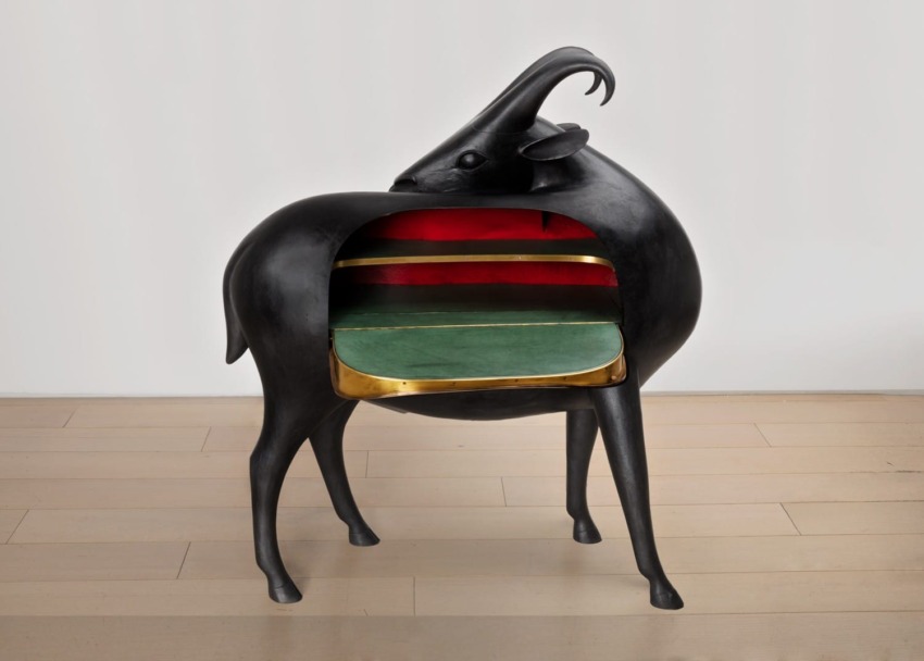 Sculptural goat-shaped cabinet with open midsection exposing colorful shelves, placed on a wooden floor.