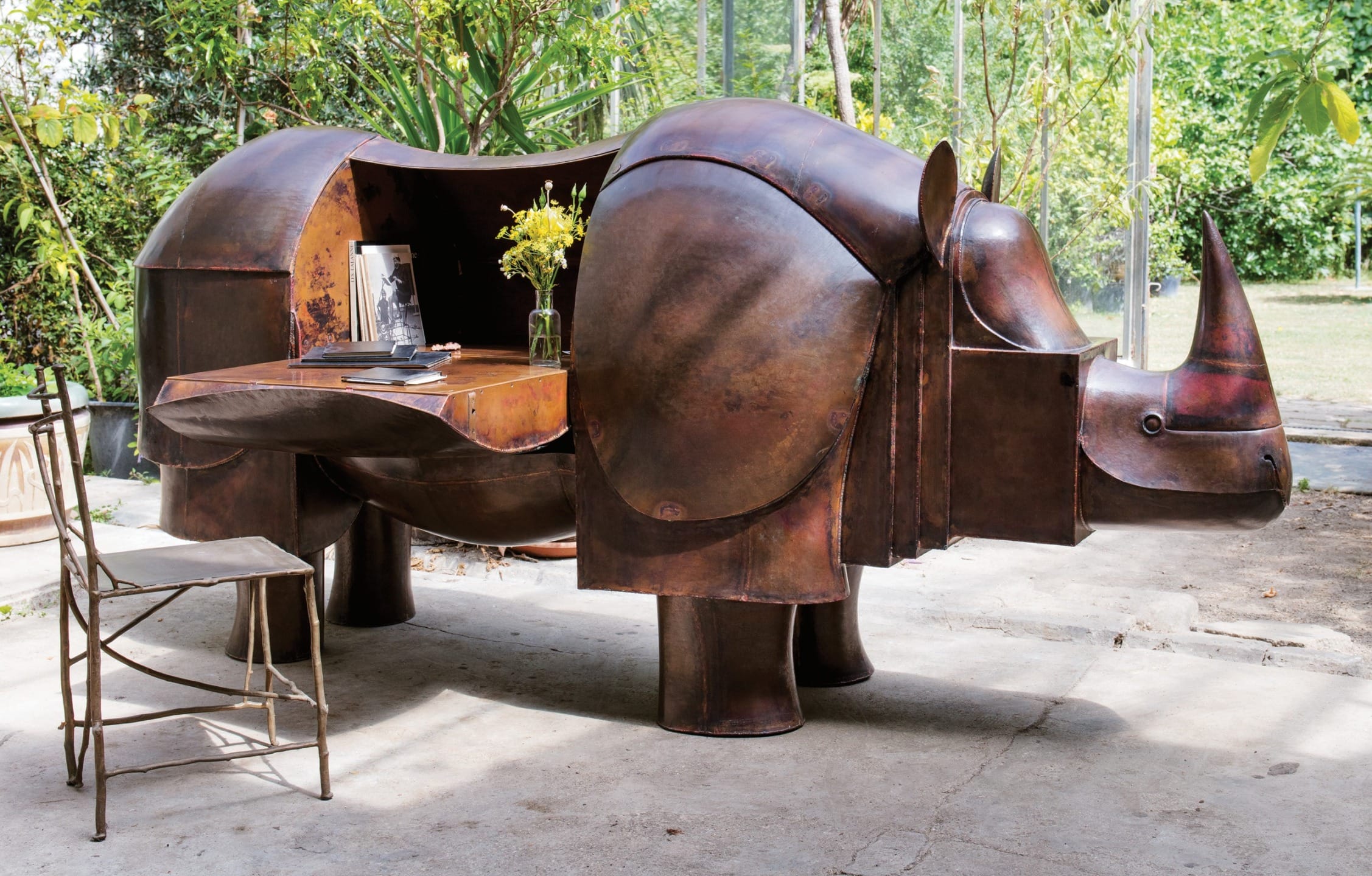 Unique rhino-shaped metal desk with open storage in garden setting featuring chair and yellow flowers on the desk