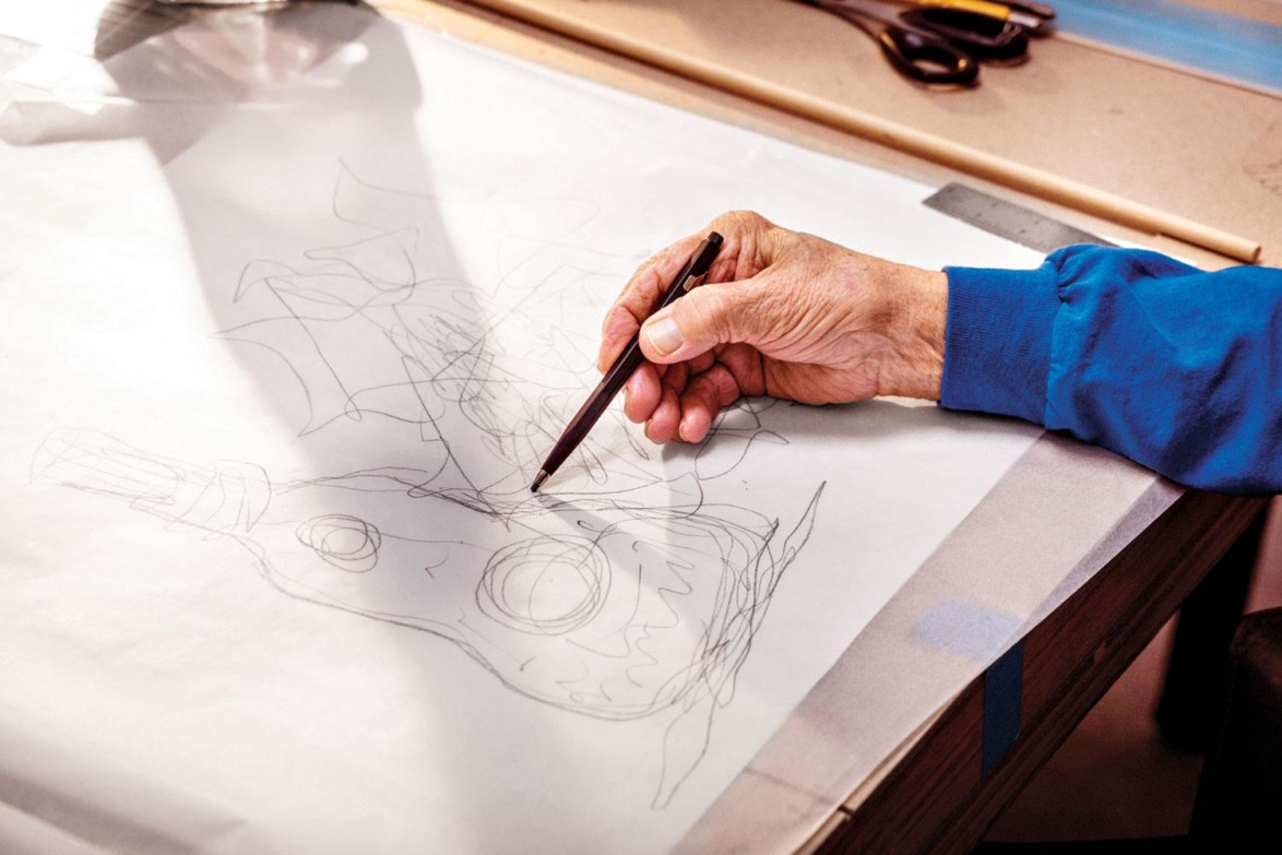 Hand sketching abstract design on paper with pencil, partially shaded by sunlight on a wooden desk.
