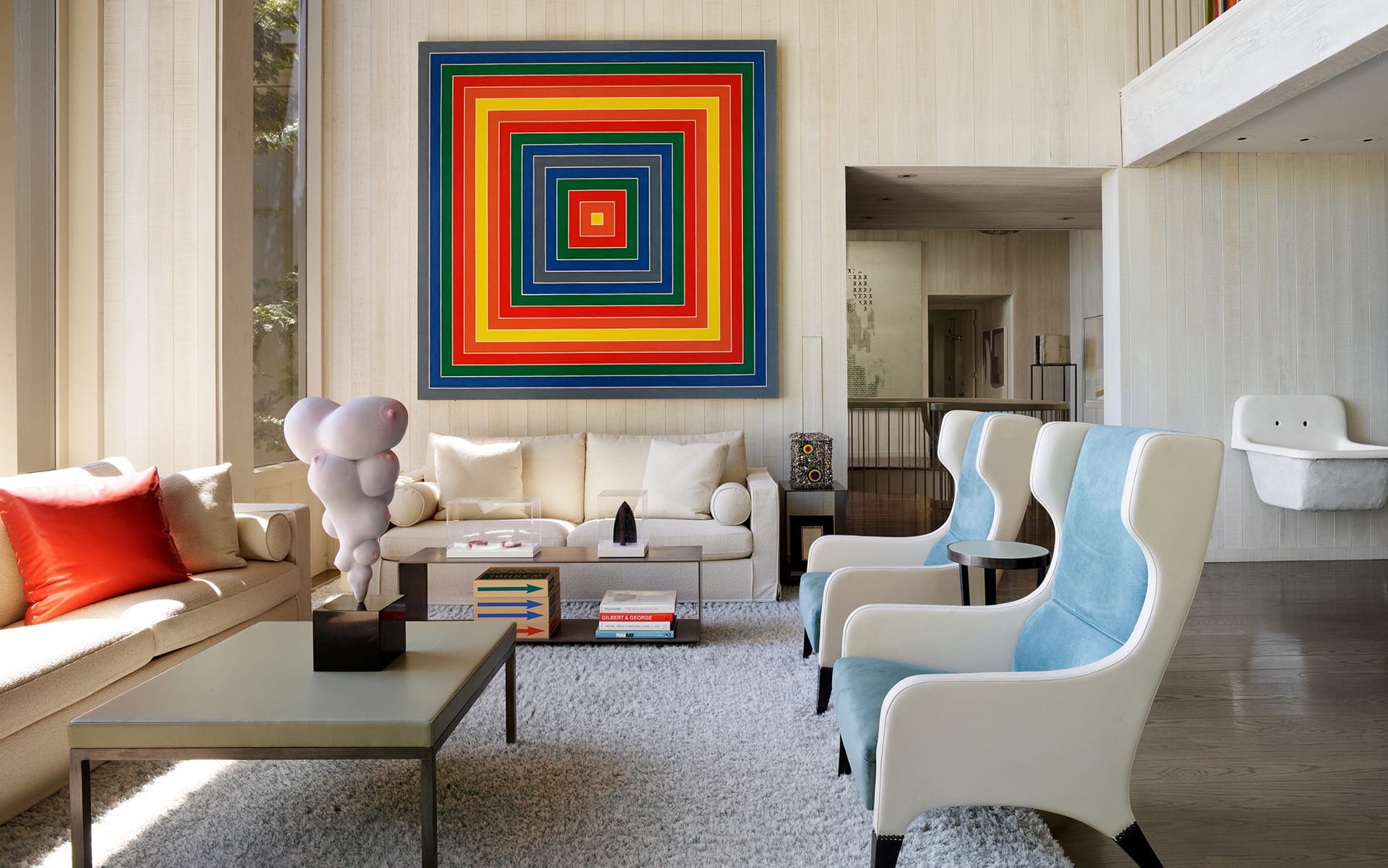 Modern living room with colorful square artwork, white and blue chairs, and a plush rug.
