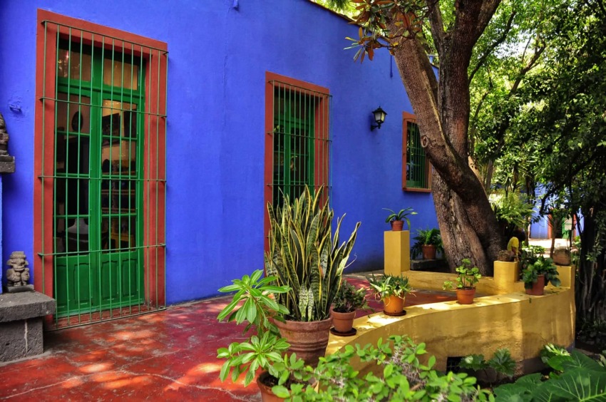 Colorful building with blue walls, green doors, and lush plants in courtyard.