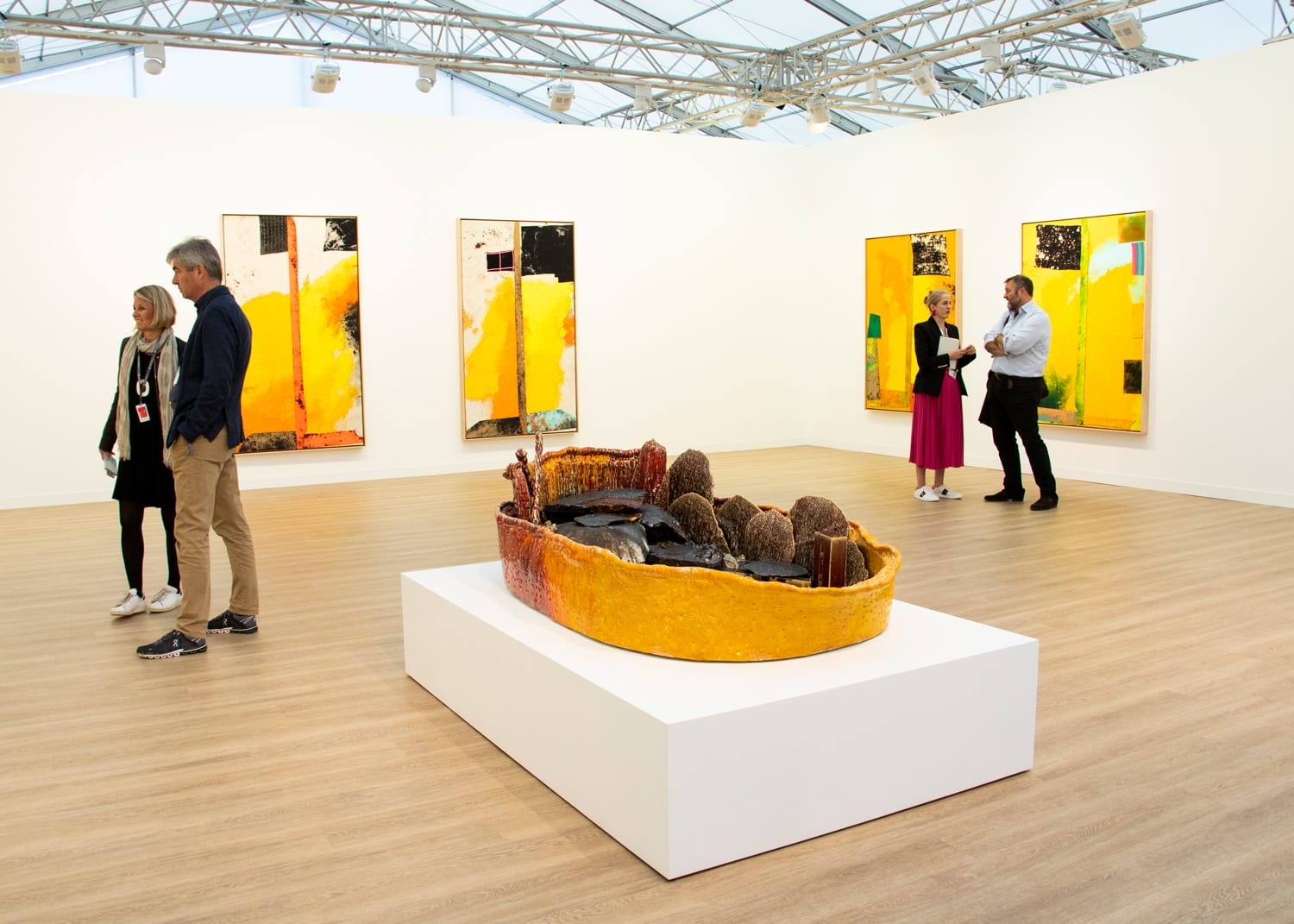 Art gallery with vibrant abstract paintings and a large ceramic sculpture, visitors observing artworks in a bright exhibition space.