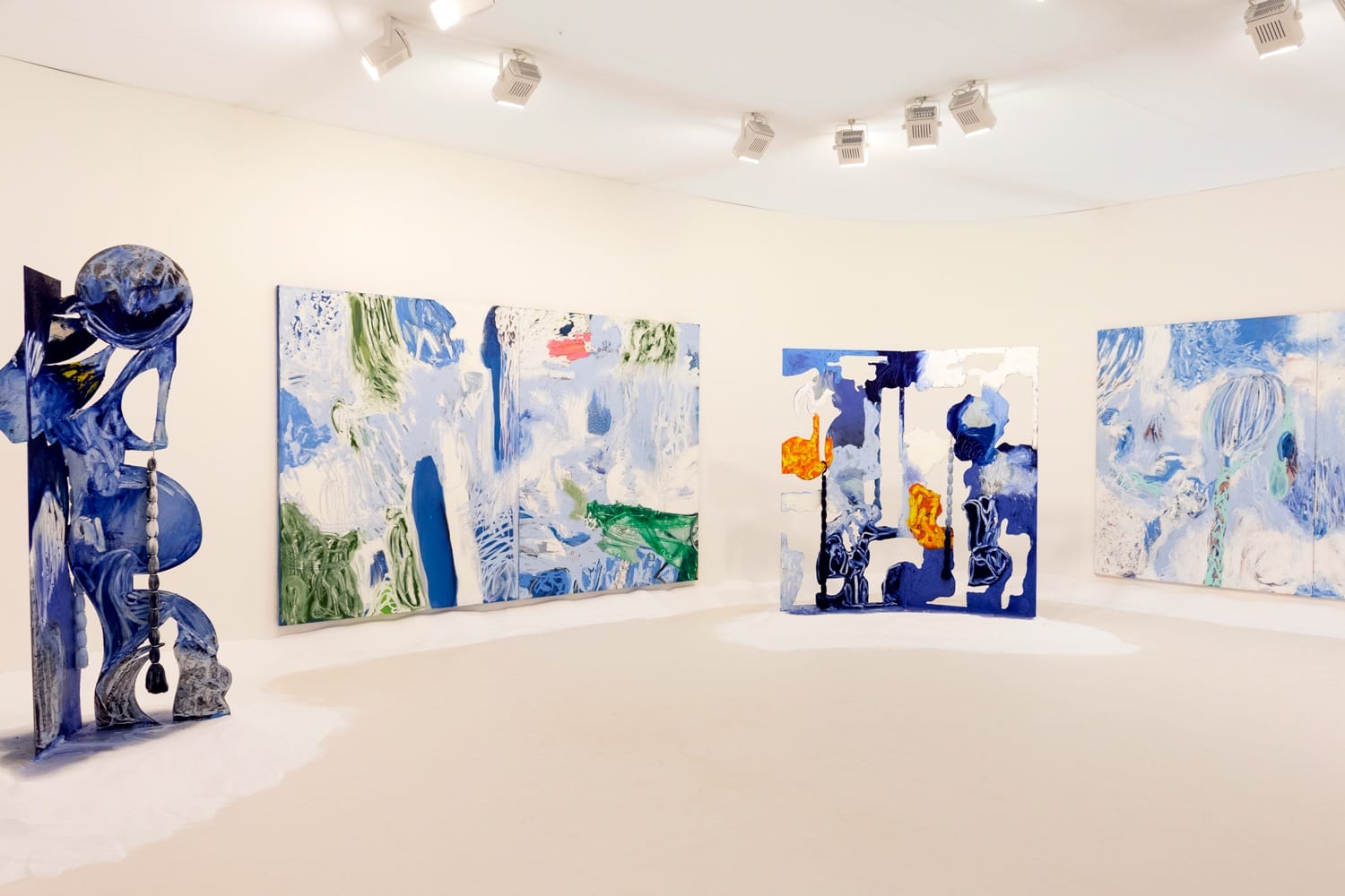 Contemporary art installation with abstract blue and white paintings and sculptures in a well-lit gallery.