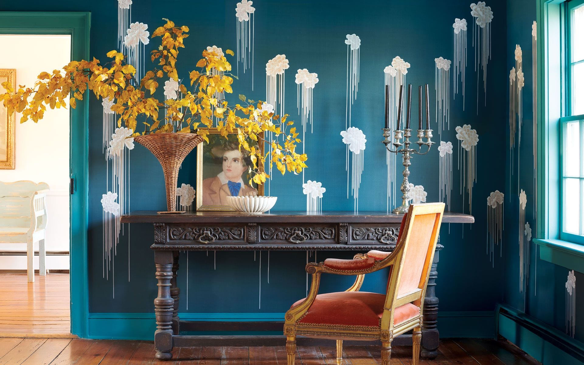 Elegant room with vintage table, ornate candle holder, flowers in a vase, a framed portrait, and an orange chair.