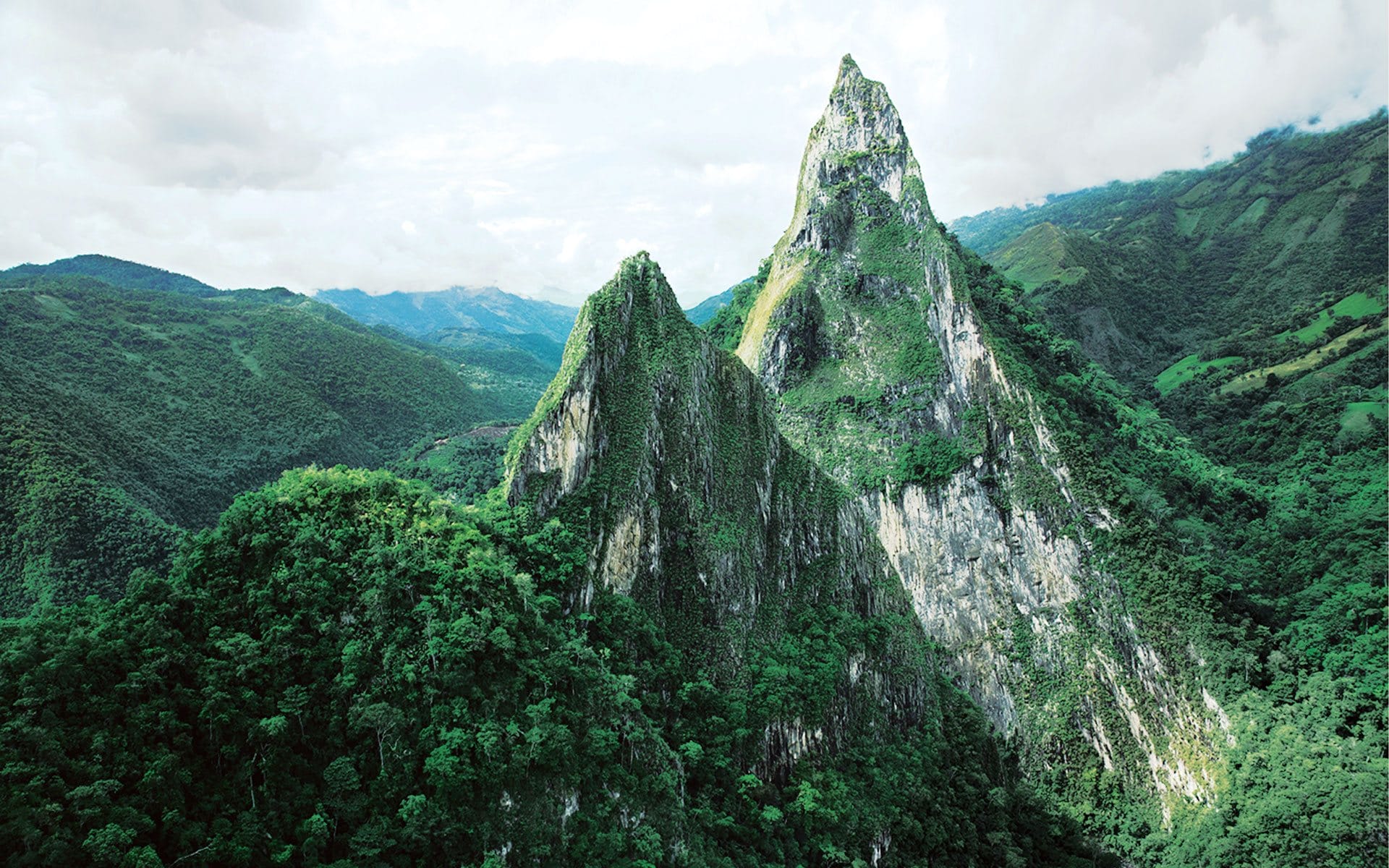 Towering green mountain peaks under a cloudy sky with lush forest covering the landscape