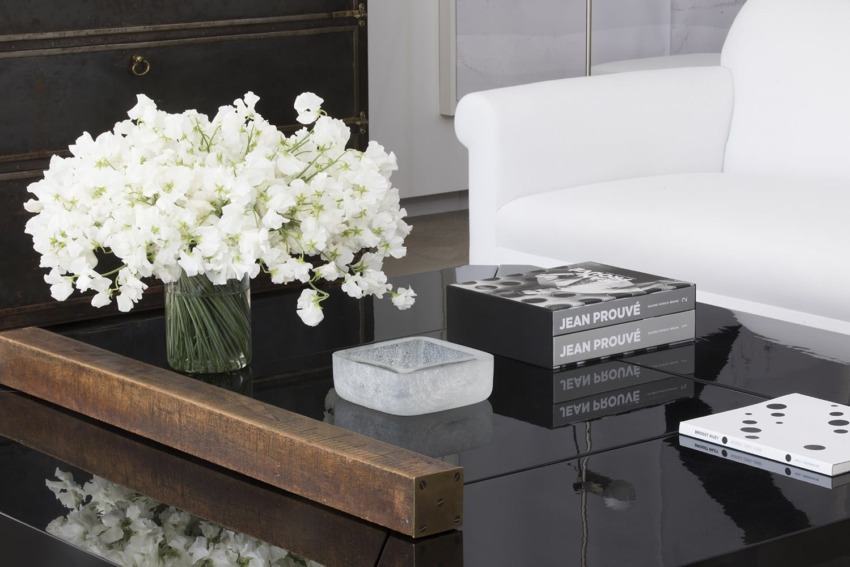 Modern living room with white flowers on a coffee table, surrounded by design books and a white sofa in the background.