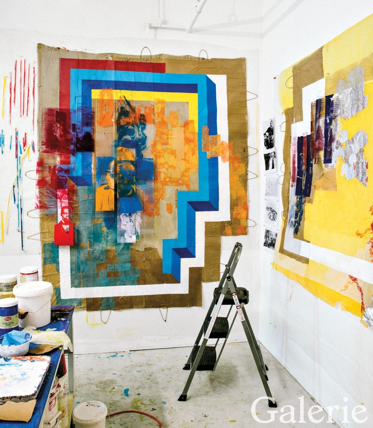 Abstract artwork with bold geometric shapes and vibrant colors on a wall in an artist's studio, adjacent to painting supplies.