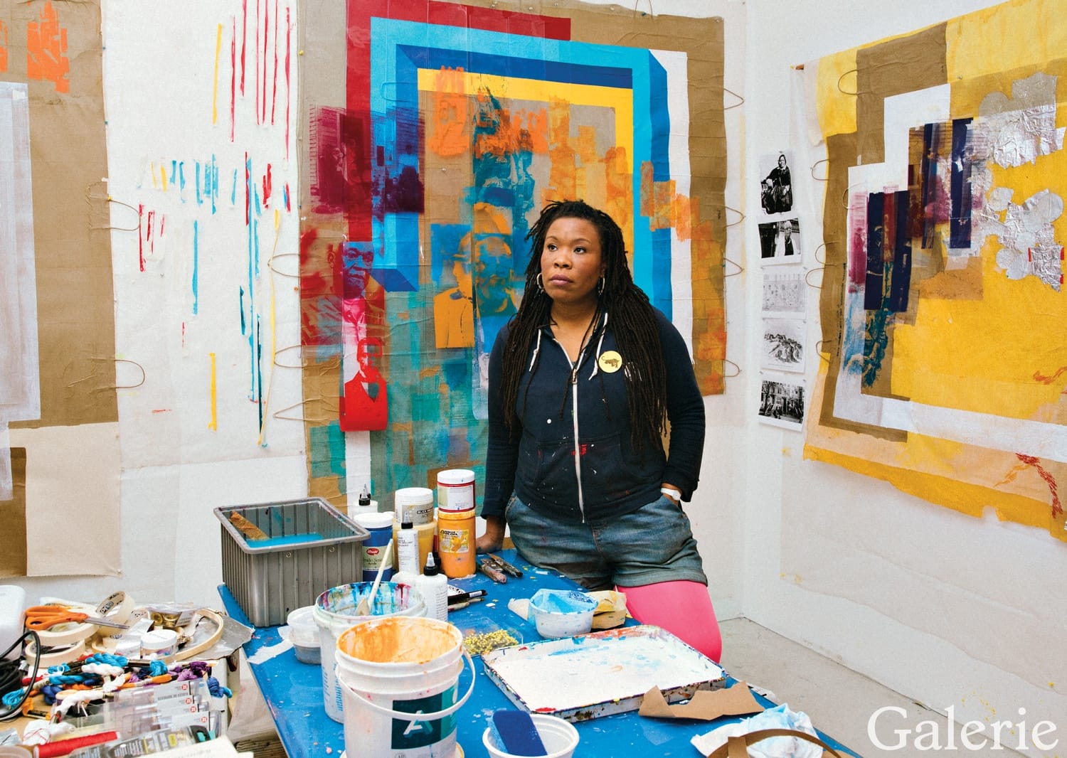 Artist in a studio surrounded by colorful abstract paintings and art supplies on the table.