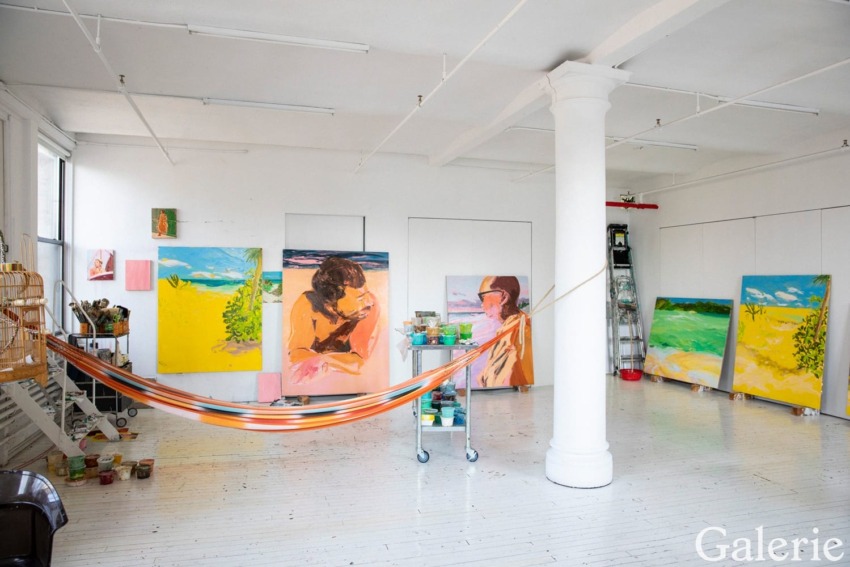 Art studio with colorful landscape paintings and a hammock, featuring a ladder and supplies in a bright, open space.